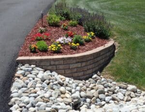 Colorful flower bed with red mulch and stone edging, showcasing low-maintenance landscaping solutions for gardens.