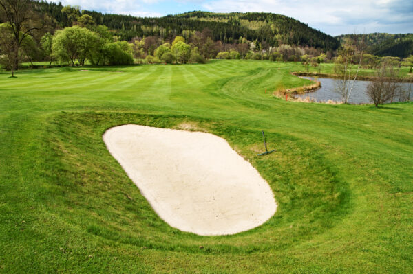 White sand bunker on the golf course, pond, wooded mountains in the background