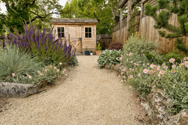 beautifully landscaped backyard with small wooden shed, fence and pathway