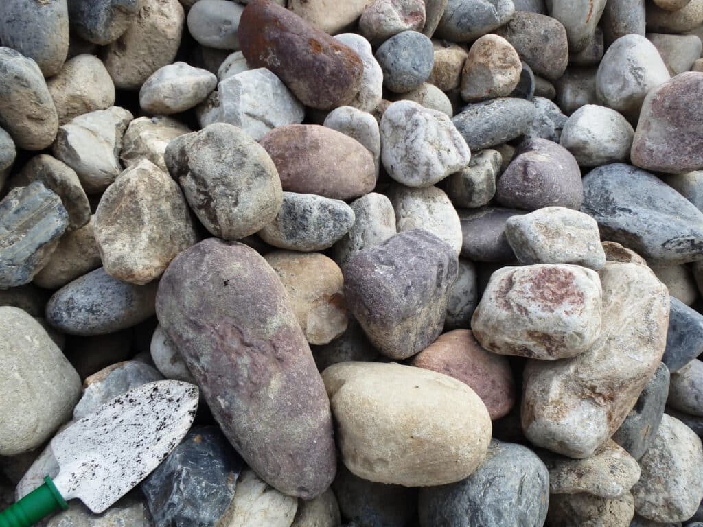 Assortment of smooth, multi-colored landscaping rocks piled together with a gardening trowel.