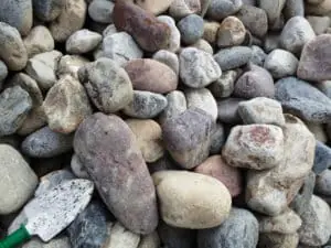 Assortment of smooth, multi-colored landscaping rocks piled together with a gardening trowel.