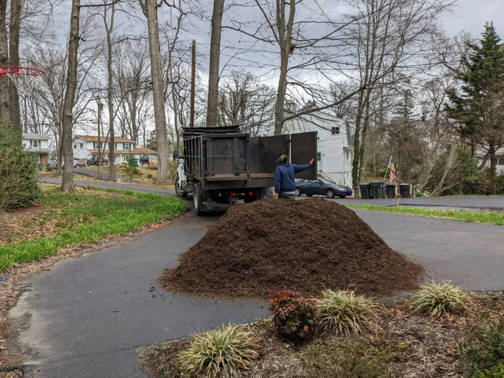 Mulch & Stone truck delivering bulk mulch to a driveway next to a flower bed